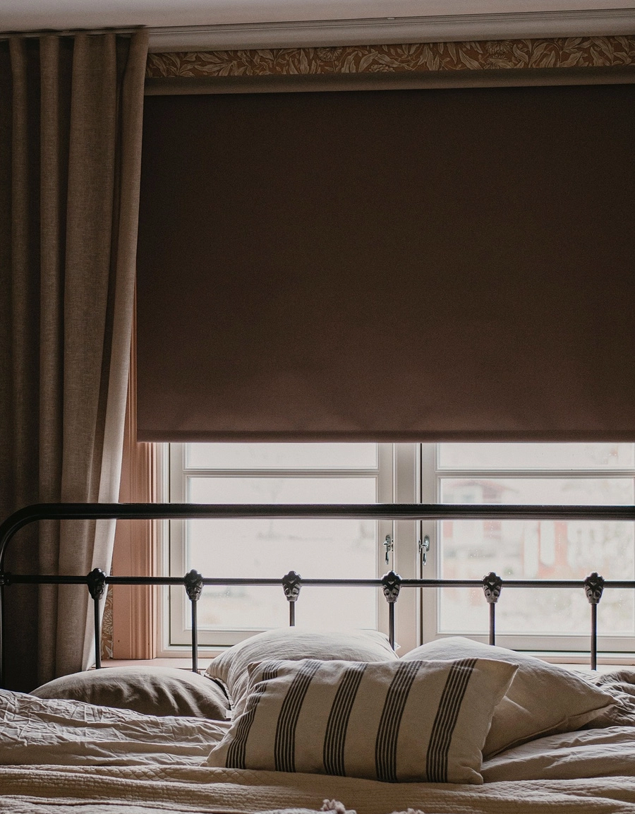 Mörkläggande brun rullgardin med beige gardinlängd i sovrum