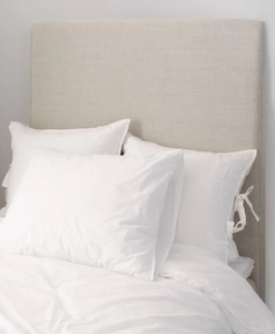 Beige sänggavel till enkelsäng med vita kuddar framför