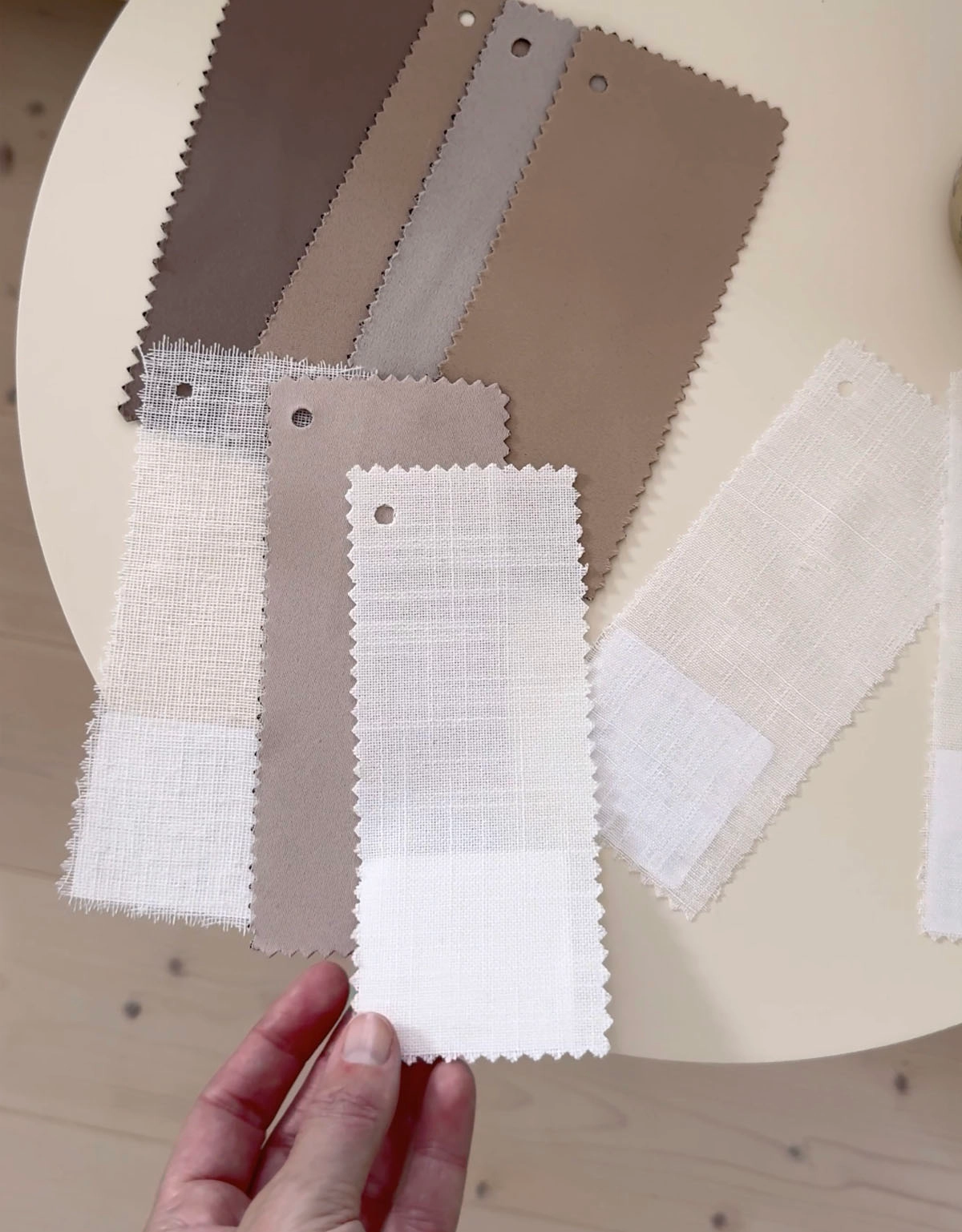 Hand som håller i ett tygprov framför ett bord med fler gardinprover