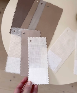 Hand som håller i ett tygprov framför ett bord med fler gardinprover