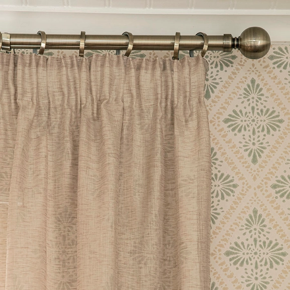 Beige gardin på gardinstång i antikmässing