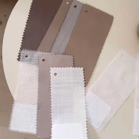 Hand som håller i ett tygprov framför ett bord med fler gardinprover