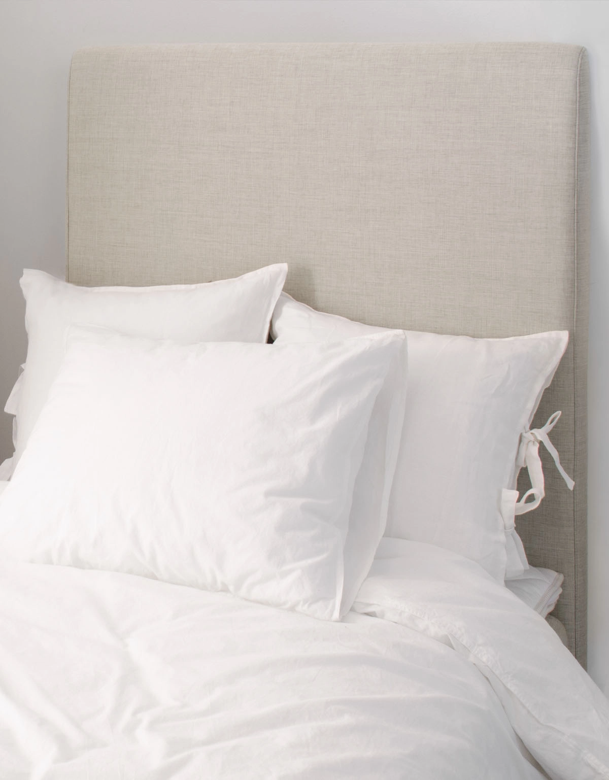 Beige sänggavel till enkelsäng med vita kuddar framför