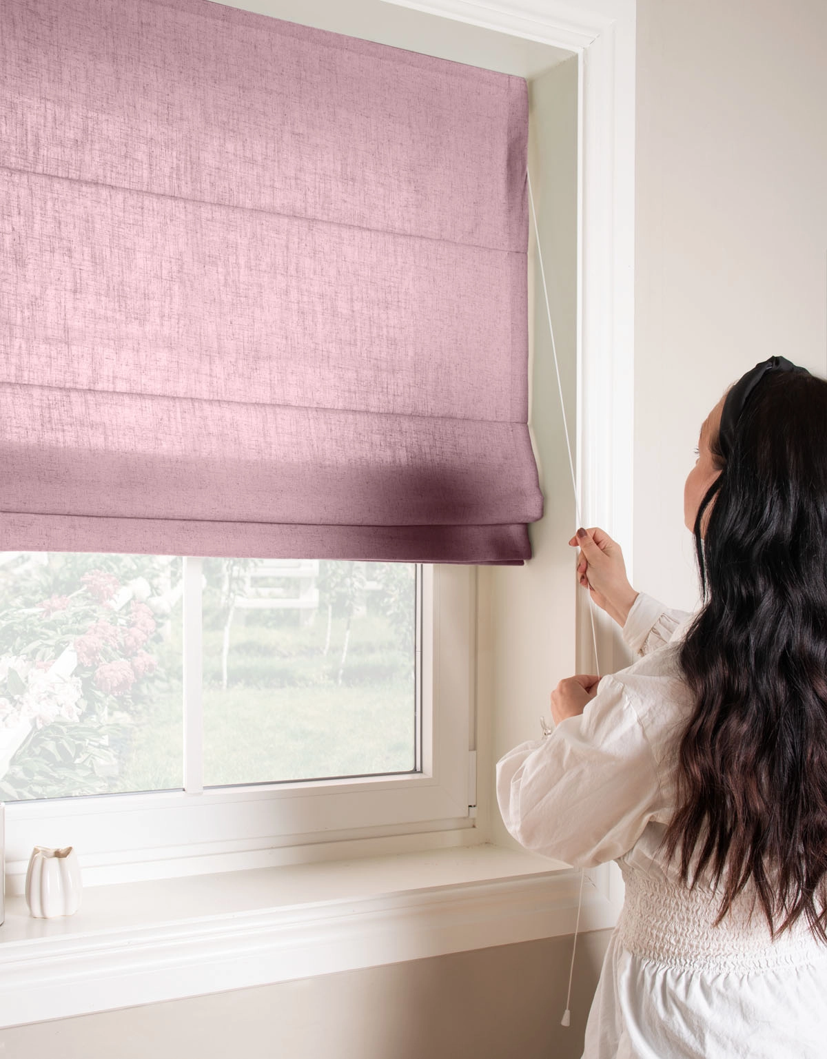 Kvinna justerar dovlila hissgardin med lina