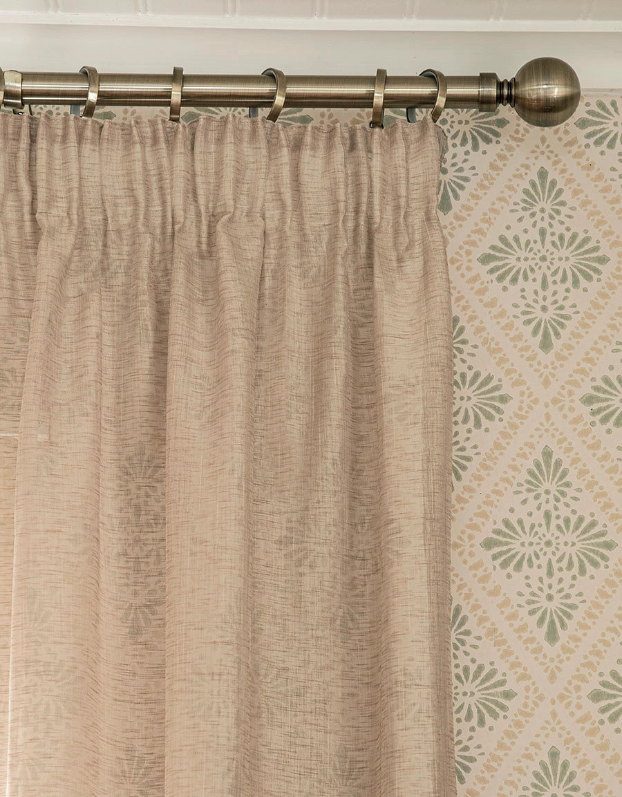 Beige gardin på gardinstång i antikmässing