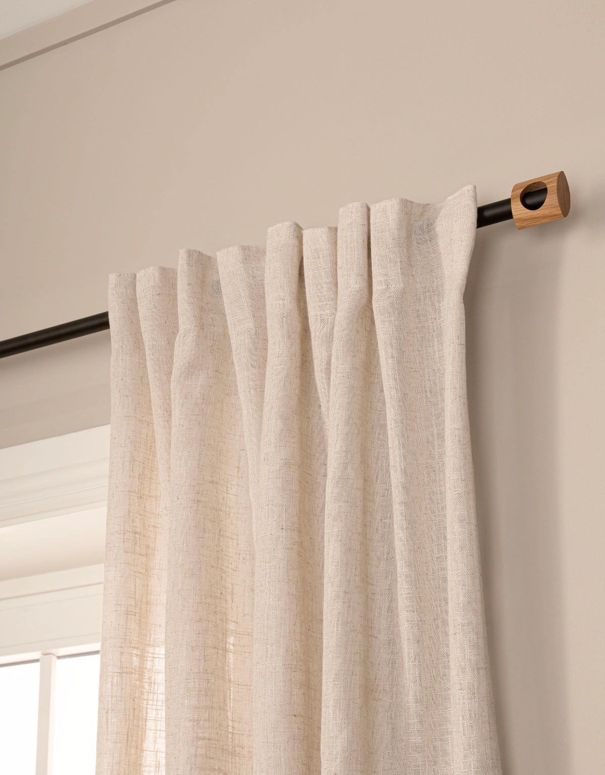Svart gardinstång med beige gardin och ändknopp i trä