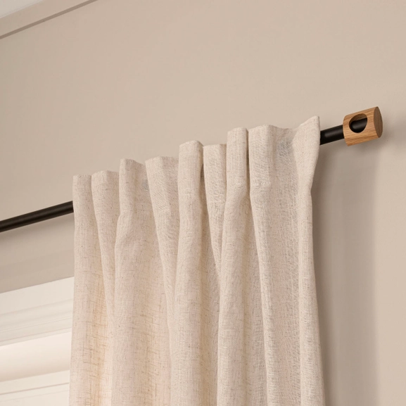 Svart gardinstång med beige gardin och ändknopp i trä