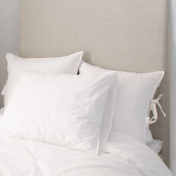 Beige sänggavel till enkelsäng med vita kuddar framför